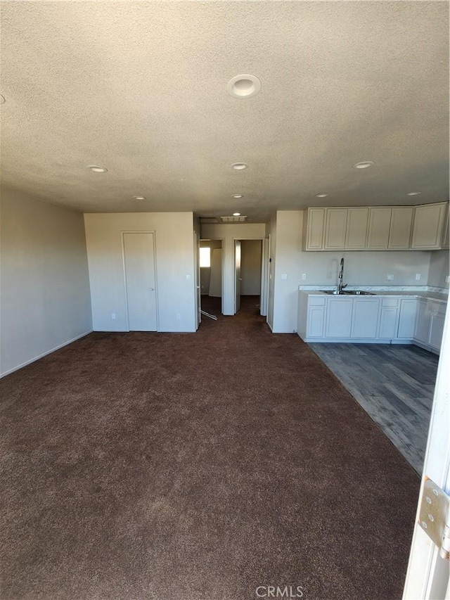 unfurnished living room with a textured ceiling, dark carpet, and sink