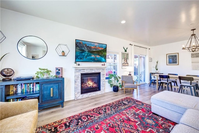 living room featuring a stone fireplace, a chandelier, and light wood-type flooring