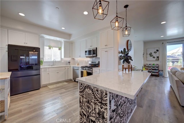 kitchen featuring light stone counters, light hardwood / wood-style flooring, appliances with stainless steel finishes, pendant lighting, and white cabinets