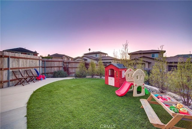 playground at dusk featuring a patio and a lawn