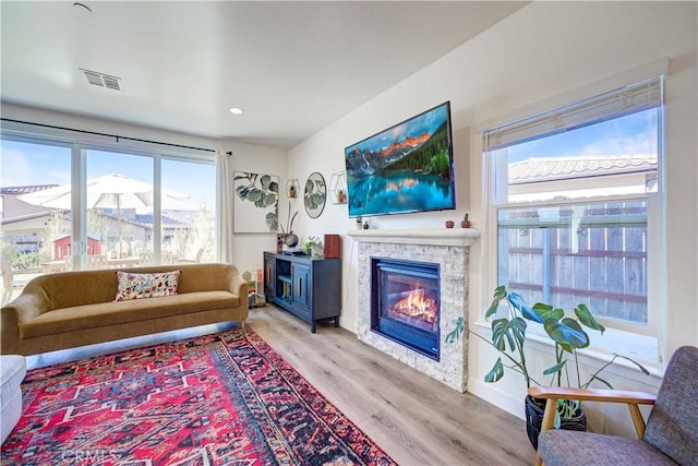 living room with a healthy amount of sunlight, a stone fireplace, and light hardwood / wood-style flooring