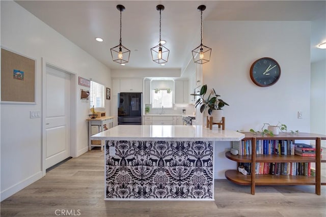 kitchen featuring black refrigerator, sink, white cabinets, hanging light fixtures, and light wood-type flooring