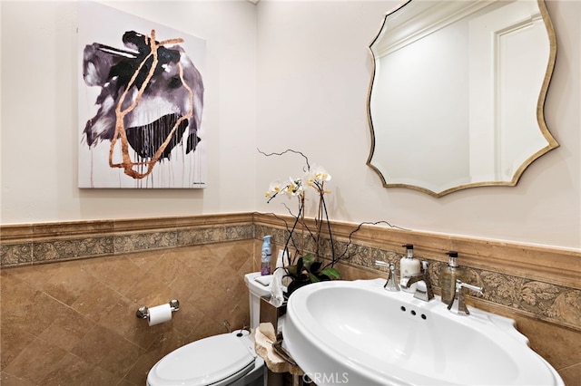 bathroom featuring a wainscoted wall, a sink, toilet, and tile walls