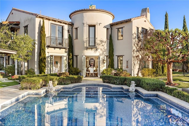 rear view of property featuring a balcony, a chimney, an outdoor pool, and stucco siding