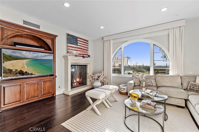 living area with a glass covered fireplace, visible vents, dark wood finished floors, and recessed lighting