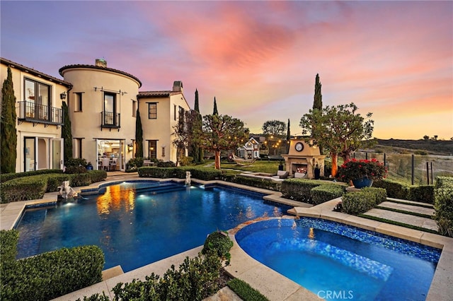 view of pool with a warm lit fireplace, a pool with connected hot tub, a patio area, and fence