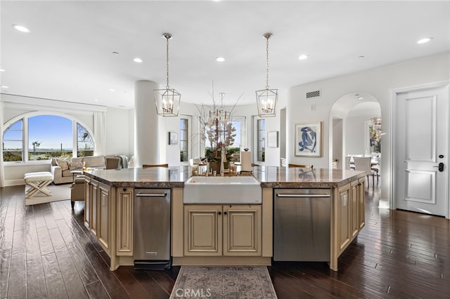 kitchen featuring arched walkways, cream cabinets, a sink, open floor plan, and stainless steel dishwasher