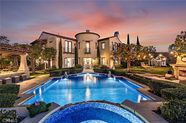 pool at dusk with a pool with connected hot tub, french doors, a patio, and a lit fireplace