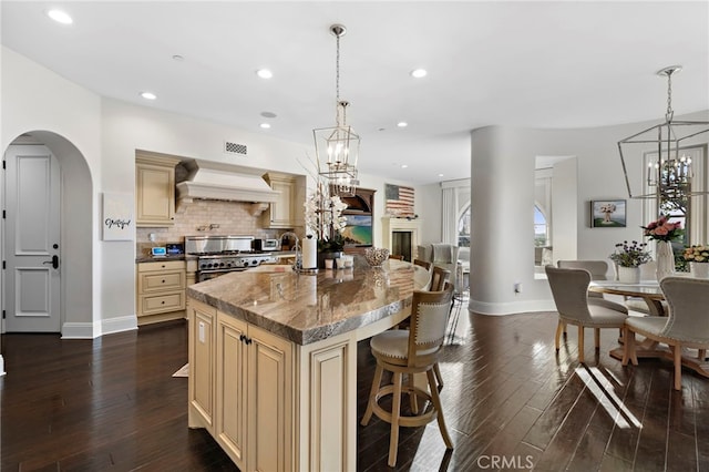 kitchen with cream cabinetry, custom exhaust hood, high end range, and a notable chandelier