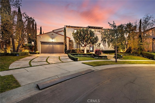 mediterranean / spanish-style house featuring an attached garage, a front lawn, concrete driveway, and stucco siding