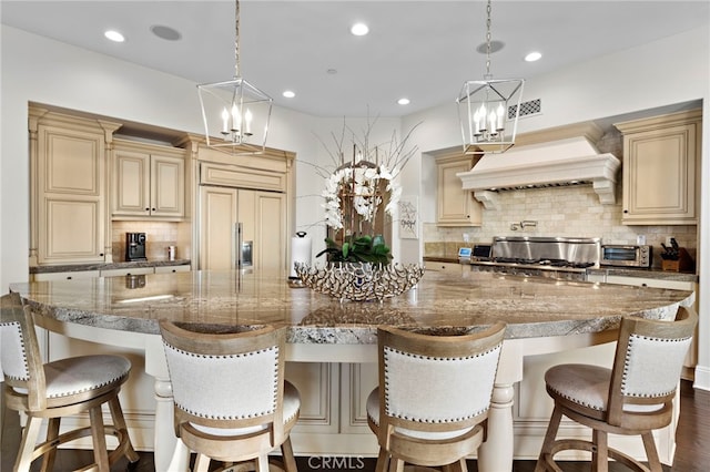 kitchen featuring cream cabinetry, custom range hood, a notable chandelier, and decorative backsplash