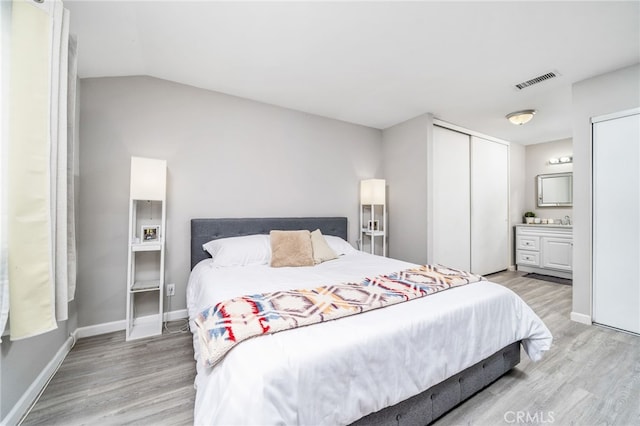 bedroom featuring light wood-type flooring, a closet, ensuite bath, and lofted ceiling