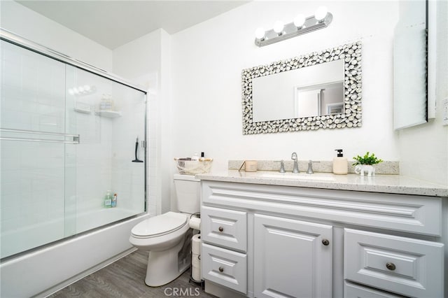 full bathroom with wood-type flooring, shower / bath combination with glass door, vanity, and toilet