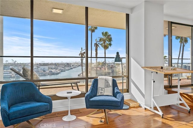 living area featuring a wall of windows, baseboards, a water view, and wood finished floors