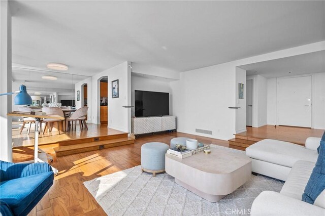 living room with visible vents, wood finished floors, arched walkways, and baseboards