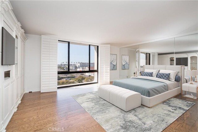 bedroom with expansive windows, crown molding, baseboards, and wood finished floors