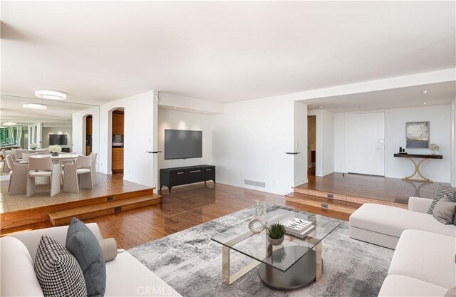 living area featuring visible vents, arched walkways, and wood finished floors