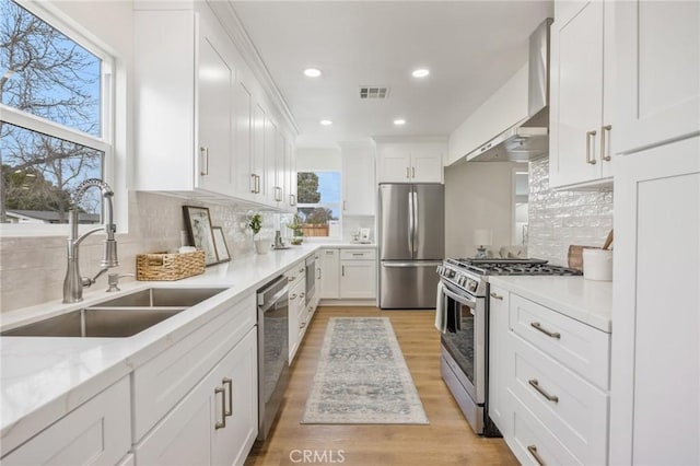 kitchen featuring sink, white cabinetry, wall chimney range hood, and appliances with stainless steel finishes