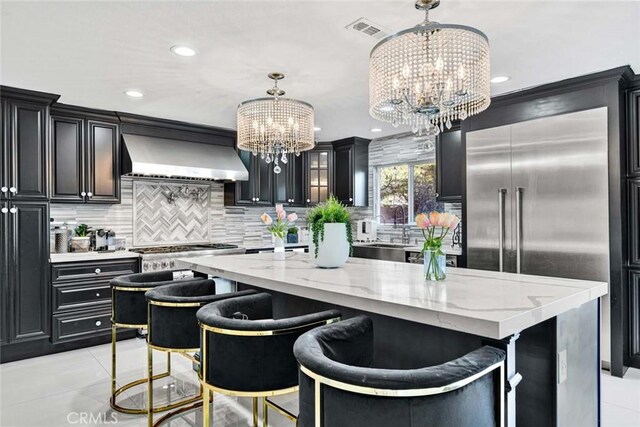 kitchen with a center island, appliances with stainless steel finishes, hanging light fixtures, wall chimney range hood, and an inviting chandelier