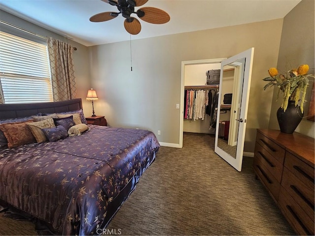 bedroom featuring a ceiling fan, dark colored carpet, a spacious closet, and baseboards