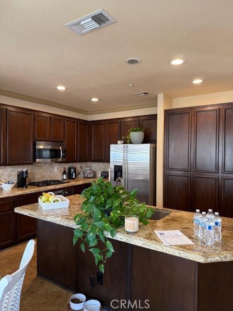 kitchen with backsplash, light tile patterned floors, dark brown cabinetry, stainless steel appliances, and light stone countertops