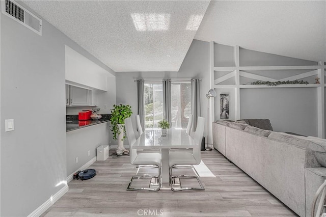 dining space featuring a textured ceiling, lofted ceiling, and light hardwood / wood-style floors