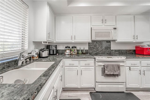 kitchen with sink, white appliances, white cabinets, and dark stone counters