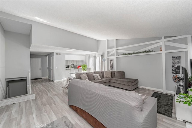 living room with lofted ceiling, light wood-type flooring, and a textured ceiling