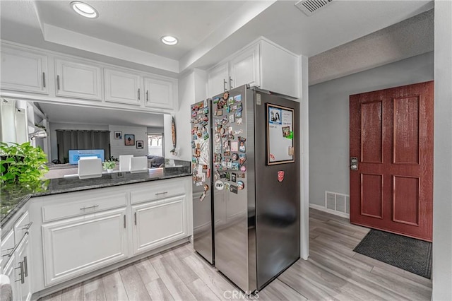 kitchen featuring white cabinetry, dark stone counters, light hardwood / wood-style floors, a raised ceiling, and stainless steel refrigerator