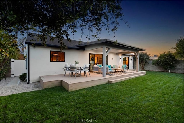 back of property at dusk featuring fence, an outdoor living space, a yard, a wooden deck, and stucco siding