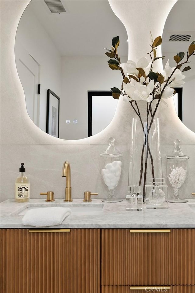 bathroom featuring visible vents, a sink, decorative backsplash, and double vanity