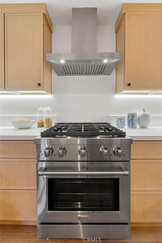 kitchen with exhaust hood, light brown cabinetry, high end range, and light hardwood / wood-style floors