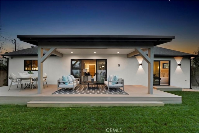 back house at dusk with a yard, outdoor lounge area, and a deck