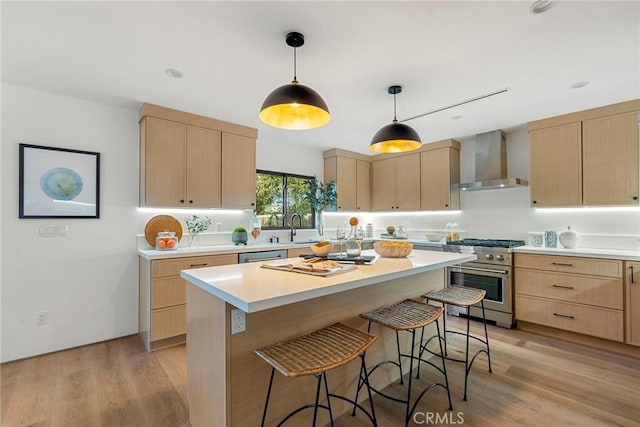 kitchen with appliances with stainless steel finishes, light brown cabinetry, hanging light fixtures, and wall chimney range hood