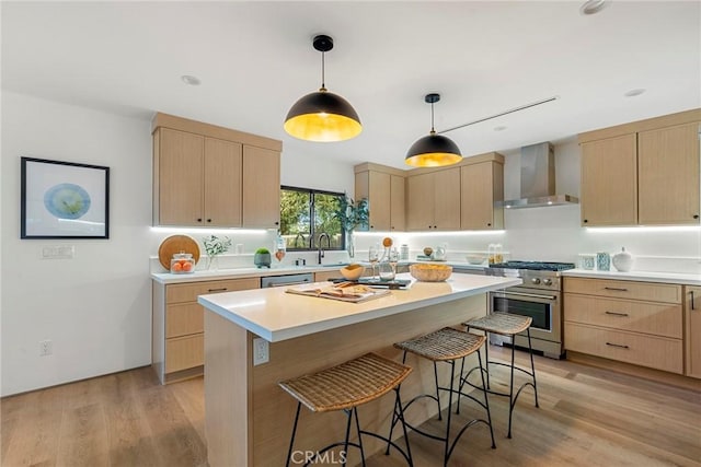 kitchen featuring appliances with stainless steel finishes, light brown cabinets, wall chimney range hood, and a kitchen bar