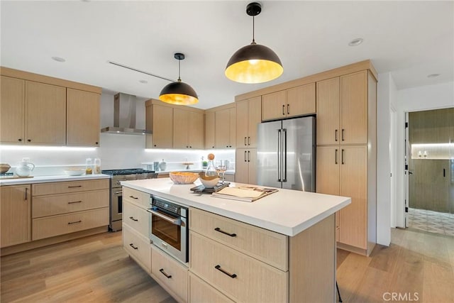 kitchen featuring light brown cabinets, high quality appliances, pendant lighting, light hardwood / wood-style floors, and wall chimney range hood