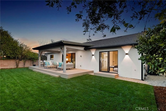 back house at dusk with an outdoor living space and a yard