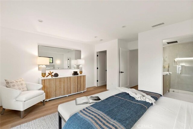 bedroom with light wood-type flooring, visible vents, and connected bathroom