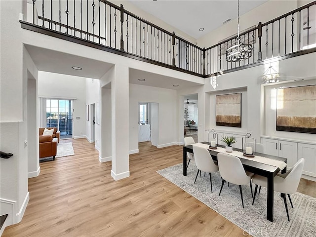 dining area with an inviting chandelier, a towering ceiling, and light hardwood / wood-style floors