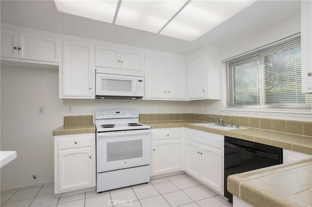 kitchen with light tile patterned flooring, sink, tile counters, white appliances, and white cabinets