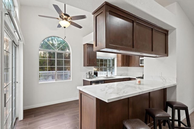 kitchen with dark wood-type flooring, dark brown cabinetry, a breakfast bar, sink, and kitchen peninsula