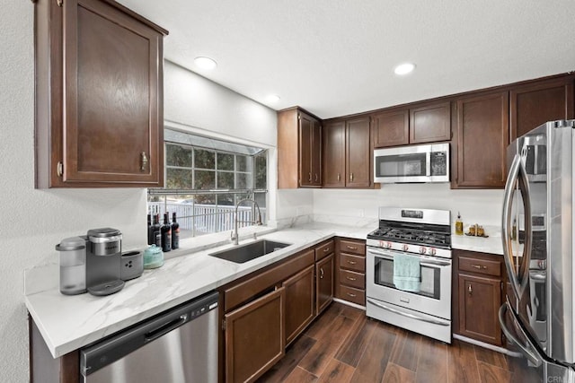 kitchen with dark brown cabinetry, sink, light stone counters, and appliances with stainless steel finishes