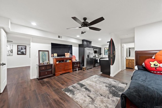 bedroom featuring stainless steel refrigerator with ice dispenser, dark wood-type flooring, connected bathroom, and ceiling fan