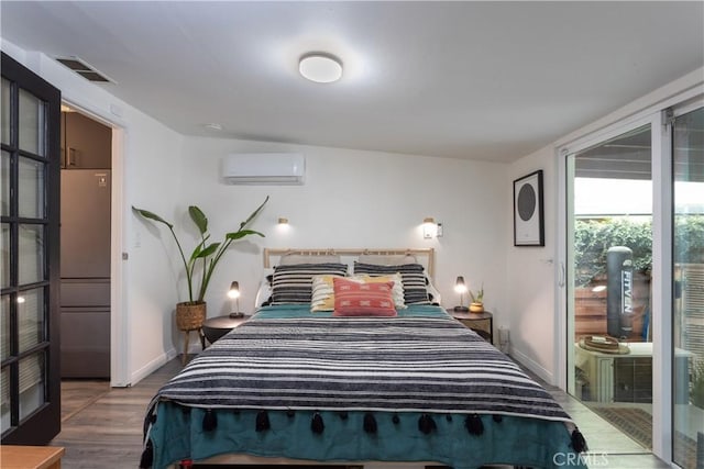 bedroom featuring an AC wall unit, stainless steel refrigerator, and wood-type flooring