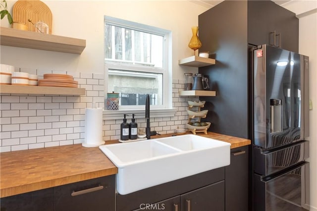 kitchen featuring stainless steel refrigerator with ice dispenser, backsplash, butcher block countertops, and sink