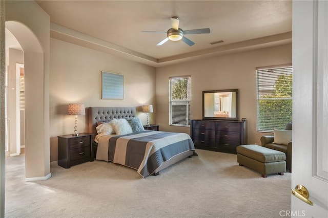 bedroom with multiple windows, a raised ceiling, light colored carpet, and ceiling fan