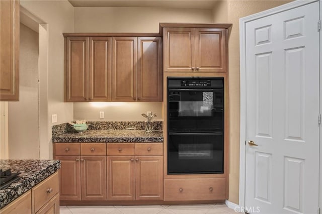 kitchen featuring light tile patterned flooring, dark stone countertops, and black appliances