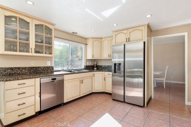 kitchen featuring stainless steel appliances, sink, cream cabinetry, and dark stone counters