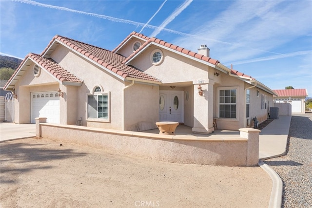 mediterranean / spanish-style home featuring a chimney, a tiled roof, an attached garage, cooling unit, and stucco siding