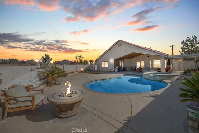 pool at dusk with an in ground hot tub, a patio area, and an outdoor fire pit